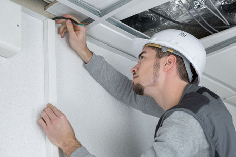 Electrician montând cabluri electrice într-un tavan fals, într-un spațiu comercial sau de birouri