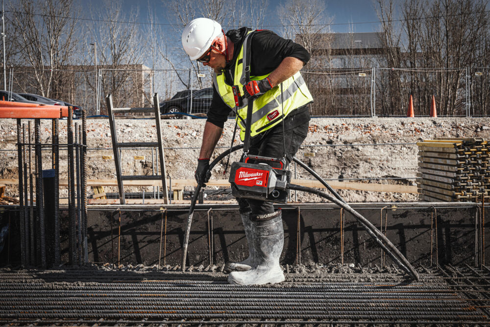 Muncitor folosind un vibrator de beton Milwaukee pentru a compacta betonul proaspăt turnat într-un cofraj armat.