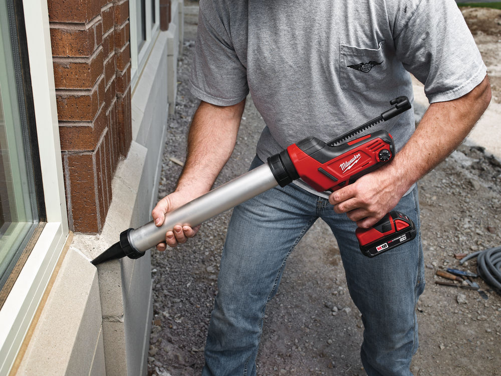 Bărbat aplicând etanșant cu un pistol electric Milwaukee M18 în rostul dintre o fereastră și peretele exterior al unei clădiri.