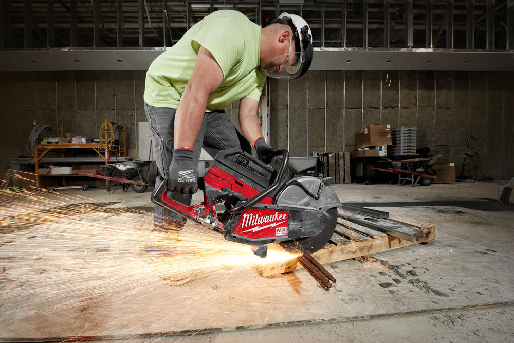 Muncitor taie bare metalice cu un polizor Milwaukee MX FUEL, generând scântei intense într-un spațiu industrial în construcție.