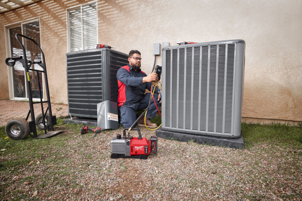 Tehnician HVAC folosind o pompă de vid Milwaukee pentru întreținerea unei unități de aer condiționat. Ideală pentru aplicații profesionale de climatizare, cu eficiență ridicată pe șantier.