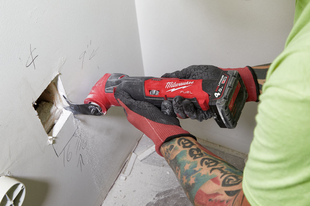 Persoană folosind un multitool Milwaukee FUEL pentru a tăia rigipsul în jurul unei deschideri dreptunghiulare într-un perete.