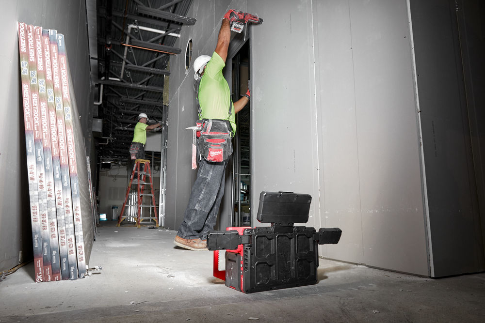 Două persoane lucrează la montarea plăcilor de rigips într-un coridor de șantier, folosind o unealtă electrică Milwaukee.
