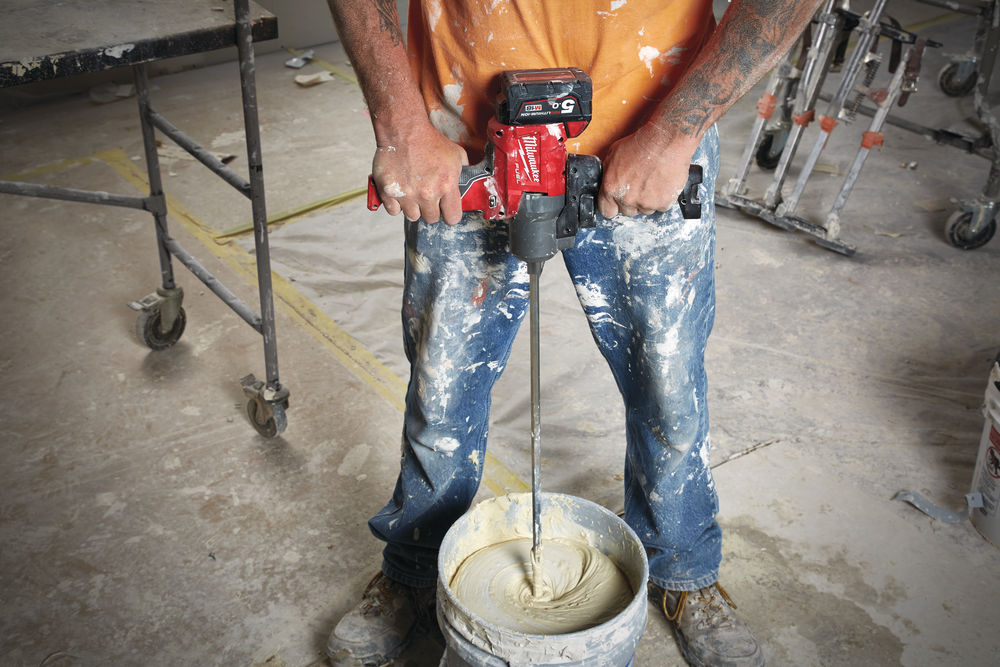 Muncitor amestecând compoziție lichidă cu un mixer electric Milwaukee, ideal pentru pregătirea rapidă a materialelor de construcții precum adezivi sau mortar.