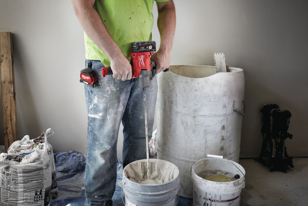 Bărbat amestecând material de construcții într-o găleată folosind un mixer electric Milwaukee cu două baterii montate.