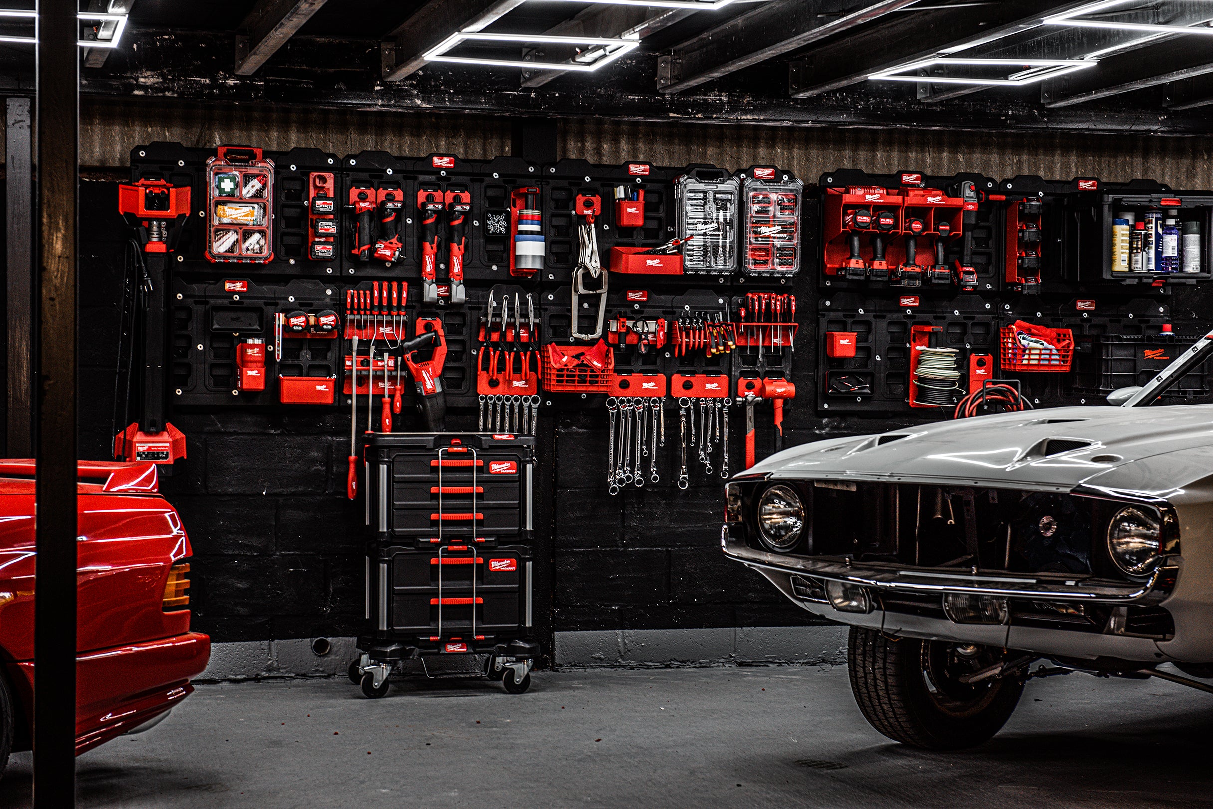 Un garaj cu o mașină roșie și una albă parcate, garajul plin cu scule Milwaukee pentru industria auto