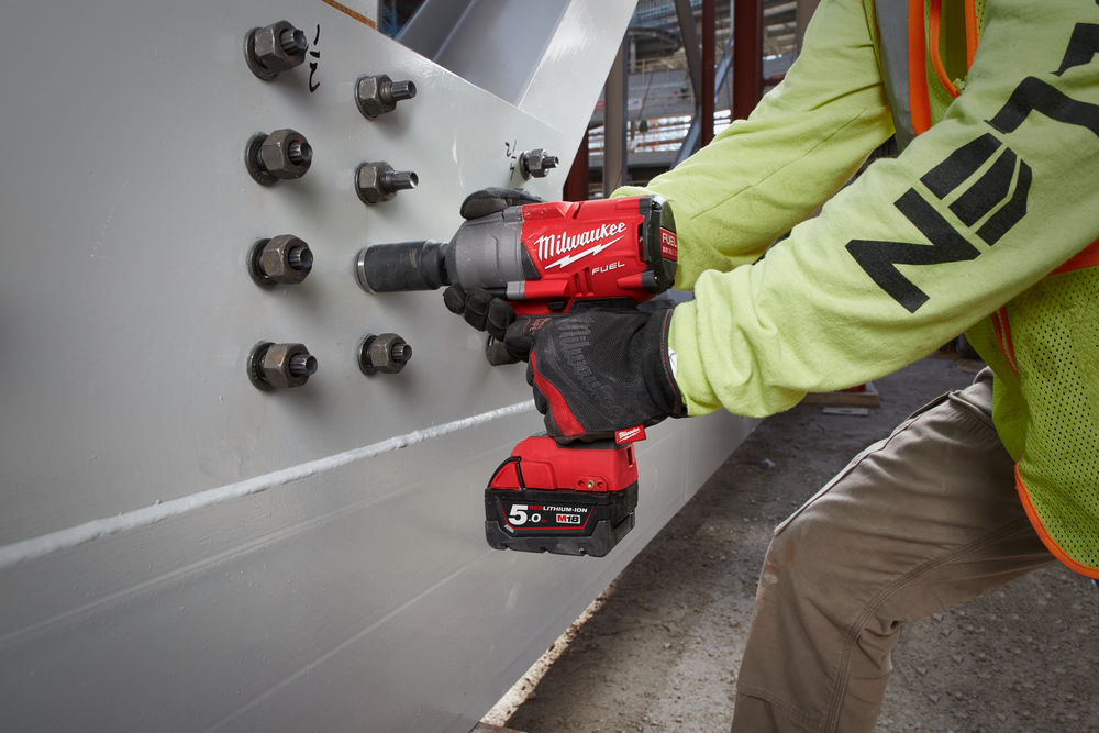 Cheie de impact Milwaukee M18 FUEL în acțiune, înșurubând șuruburi de mari dimensiuni într-o grindă metalică.