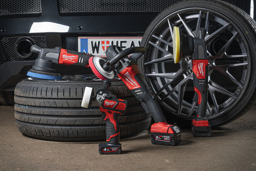 Mai multe scule Milwaukee fără fir pentru polish și lustruire auto, așezate lângă roți și anvelope auto, inclusiv o mașină de polish, un șlefuitor și o bormașină cu acumulatori REDLITHIUM.