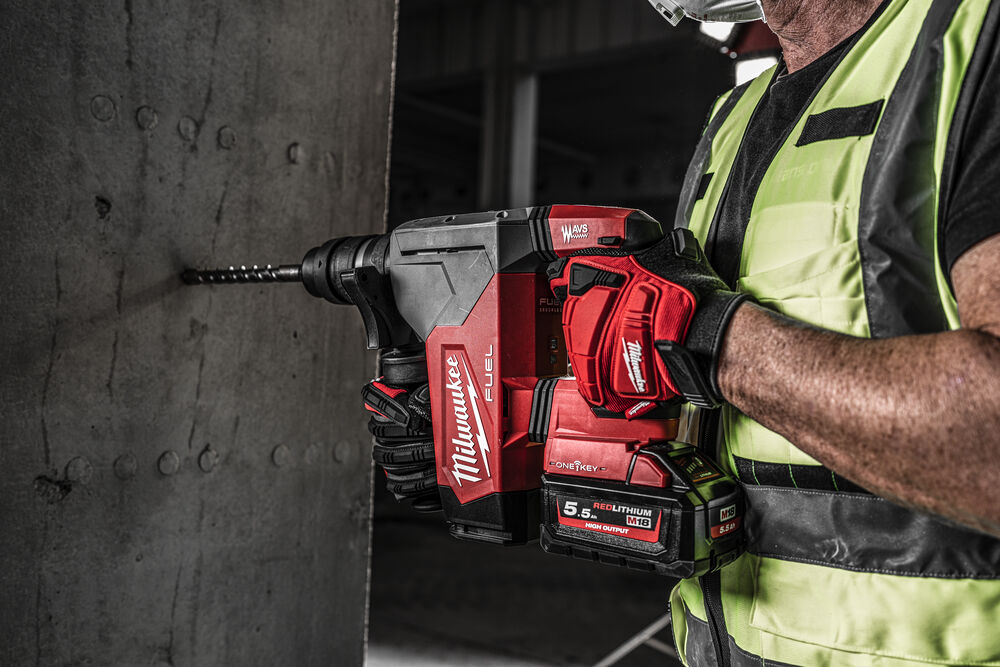 Muncitor perforând un perete de beton cu un ciocan rotopercutor Milwaukee FUEL echipat cu baterie REDLITHIUM M18 și mănuși de protecție Milwaukee.